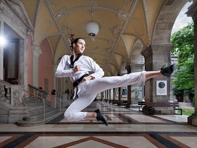 Frau macht einen Sprungkick im Taekwondo-Outfit